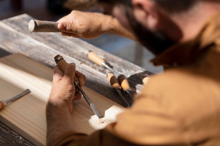 Close-up of a craftsperson shaping wood with a chisel at a workbench.