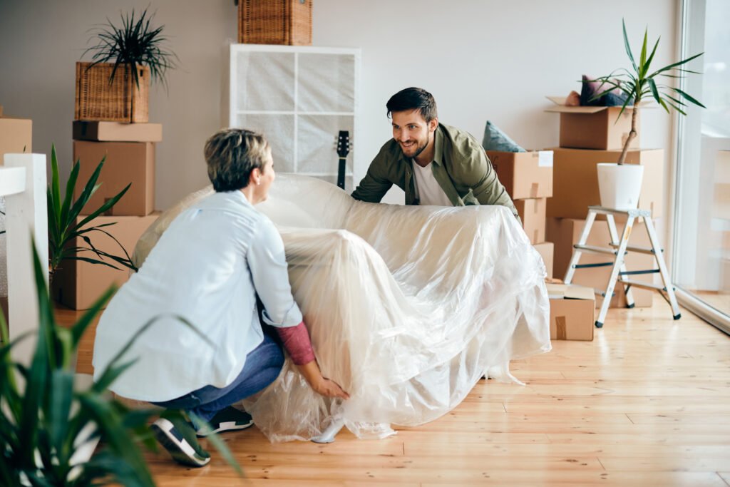 Two people unpacking a sofa in a bright room with moving boxes.