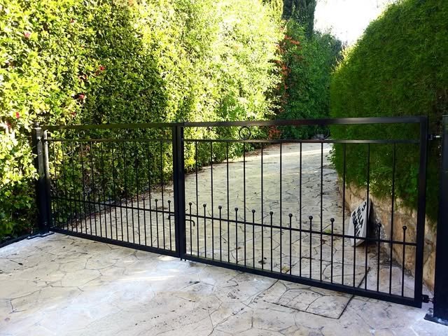 Custom black metal driveway gate beside a landscaped entrance